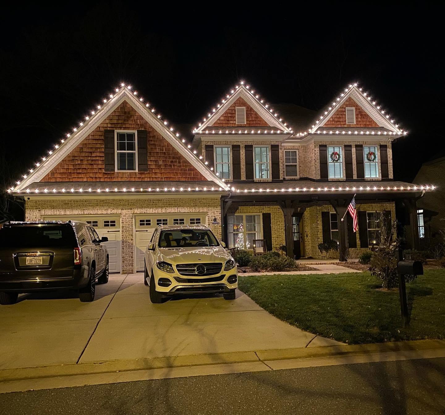 Real installation on a brick home with warm white lights along the roof peaks and Christmas decorations at the porch